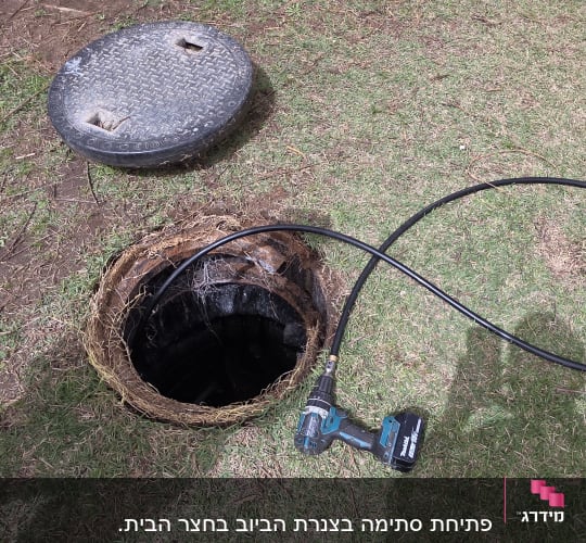 בור ביוב פתוח עם מכסה וכלי עבודה על הדשא